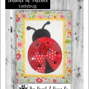 May include: A red and black ladybug quilt block with a floral border. The quilt block is made of fabric scraps and has a patchwork design. The title "Seasons in Patches Ladybug" is at the top of the image. The Heart & Home Co. logo is at the bottom of the image.