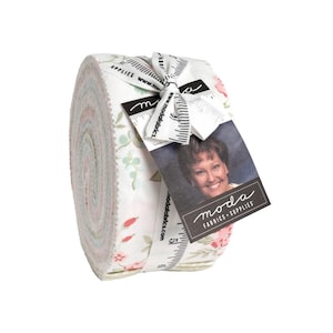 May include: A rolled bundle of fabric with a floral pattern in shades of pink, green, and white. The fabric is tied with a white ribbon and a tag featuring a woman's photo and the words "moda FABRICS + SUPPLIES".