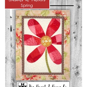 May include: A quilt block featuring a red and pink flower with a yellow center. The block is surrounded by a floral border and is titled "Seasons in Patches Spring". The quilt block is made by The Heart & Home Co.