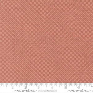 May include: A close-up of a fabric with a repeating pattern of small, light-colored circles on a coral-colored background. The fabric has a textured appearance. A ruler is at the bottom, with measurements in inches.