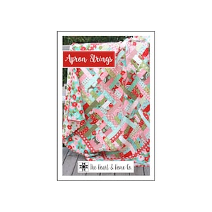 Puede incluir: Un patrón de colcha llamado "Apron Strings" de The Heart & Home Co. La colcha está hecha con una variedad de telas en tonos de rojo, rosa, verde y azul. La colcha está colgada en una valla de madera.