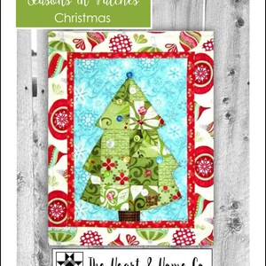 May include: A Christmas-themed quilt with a patchwork Christmas tree design. The tree is green with decorative buttons and sits on a blue background with snowflake patterns. The quilt is framed with a red border and festive ornaments. The text "Seasons in Patches Christmas" is at the top.