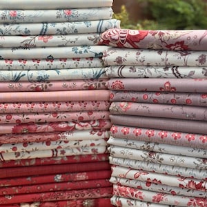 May include: Two stacks of folded fabric featuring a variety of floral and botanical patterns in shades of red, pink, cream, and muted blue. The textiles display intricate designs including small blossoms, vines, and larger floral motifs.