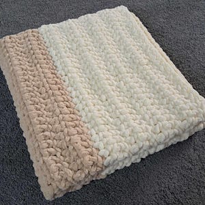 May include: A folded, plush blanket with a two-tone design. One side is a soft beige, and the other is a creamy white. The blanket has a thick, textured appearance, suggesting a cozy and warm feel. Ideal for home decor and comfort.