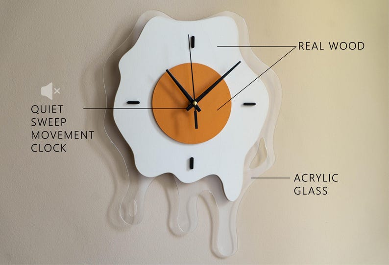 May include: A quirky wall clock in the shape of a fried egg, with a white egg white and an orange yolk. It has black hands and markers, made from real wood and acrylic glass. The text "QUIET SWEEP MOVEMENT CLOCK" is displayed on the left.