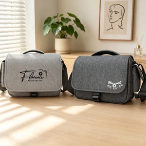 May include: Two rectangular camera bags with top handles and adjustable shoulder straps. The left bag is light gray with black text reading Florence Photography and a camera icon. The right bag is dark gray with white text reading Hannah.