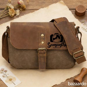 Puede incluir: Bolso mensajero de lona marrón y verde oliva con solapa y correa de cuero. El bolso presenta un logotipo de cámara con el nombre "Samantha Photography" impreso en negro. El bolso tiene un cierre de hebilla y una correa de hombro ajustable.