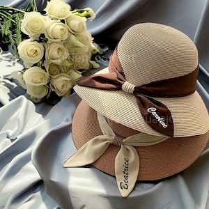 May include: Two straw hats with brown ribbon ties. The top hat has the name "Caroline" written on the ribbon. The bottom hat has the name "Beatrice" written on the ribbon.