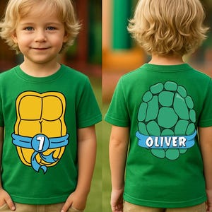 May include: A green t-shirt featuring a yellow turtle shell design with a blue ribbon and the number 7. The back of the shirt displays a green turtle shell design with the name "OLIVER" on a blue ribbon. The shirt is worn by a young child.