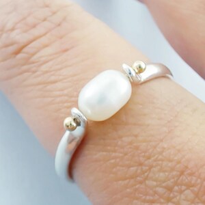 May include: A silver ring with a white pearl and gold accents.