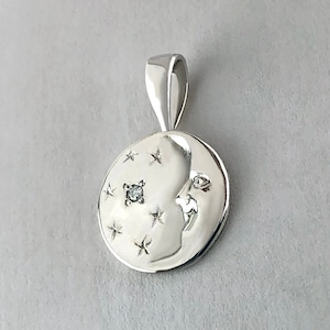 May include: Silver pendant featuring a crescent moon with a face and a small diamond in the center. The moon is surrounded by small stars.