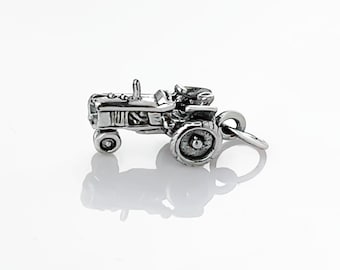 May include: A small, silver tractor charm with detailed features, including wheels, a seat, and a steering wheel. The charm has a loop for attaching to a bracelet or necklace. The tractor is a miniature replica of a farm vehicle.