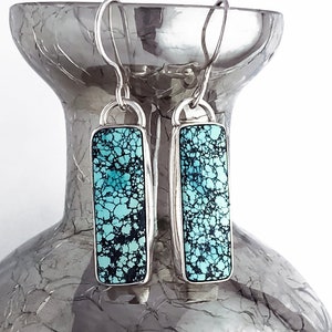 Puede incluir: Un par de pendientes de plata con piedras turquesa. Las piedras son de color azul claro con vetas negras.