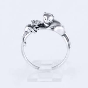 May include: A silver ring featuring a sculpted design of two cats, one larger cat with a smaller cat nestled on its back.