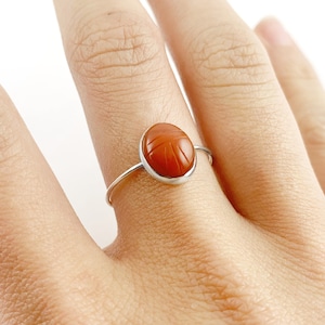 May include: A silver ring with a red carnelian stone featuring a carved scarab beetle design.