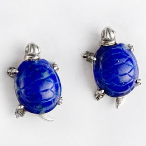 May include: A pair of silver turtle earrings with blue lapis lazuli stones.
