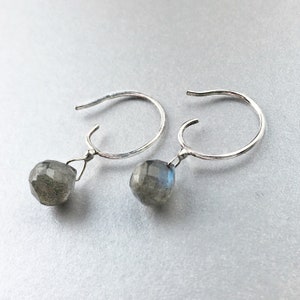 Peut inclure: Une paire de boucles d'oreilles créoles en argent avec une pierre de labradorite grise suspendue à chaque boucle d'oreille.