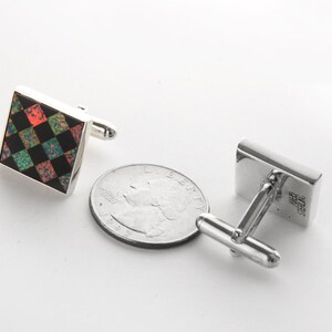 May include: A pair of silver cufflinks with a square black and green checkered design with red accents. The cufflinks are about the size of a US quarter.