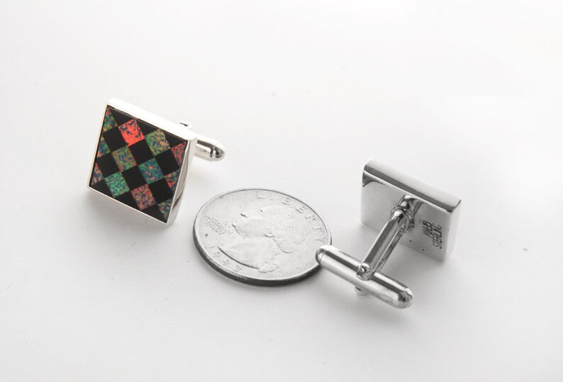 May include: A pair of silver cufflinks with a square black and green checkered design with red accents. The cufflinks are about the size of a US quarter.