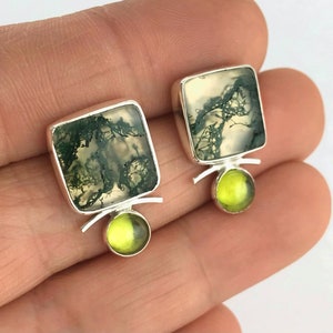May include: A pair of silver earrings with square green moss agate stones and round green peridot stones.