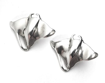 Könnte beinhalten: Ein Paar silberne Ohrringe in Form von Mantarochen. Die Ohrringe sind detailliert und haben eine glatte, polierte Oberfläche.