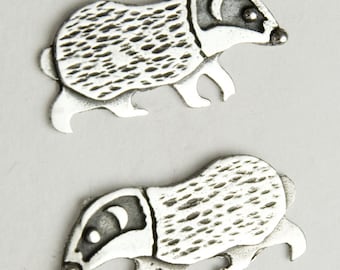 May include: Two silver badger figurines, each with a detailed textured body and a black eye. The badgers are walking in a side view position.
