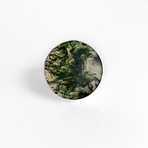 May include: A silver ring featuring a round green and white moss agate stone.