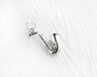 May include: A silver charm in the shape of a saxophone. The charm has a loop at the top for attaching to a bracelet or necklace.