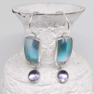 May include: A pair of silver dangle earrings with iridescent blue and purple stones. The earrings feature a rectangular shaped stone with a smaller round stone dangling below.