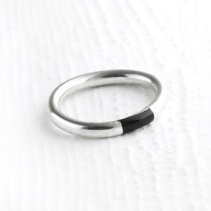 Peut inclure: Une bague en argent avec une incrustation noire. La bague est simple et élégante.
