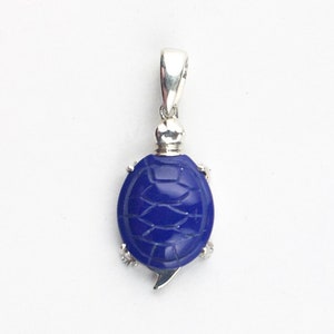 Può includere: Ciondolo in argento con un design a tartaruga blu scolpita. La tartaruga ha un motivo a guscio dettagliato e piccoli accenti argentati per le pinne. Il ciondolo ha un'ansa in argento per il fissaggio a una catena.