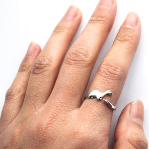 A handmade adjustable ring of a dinosaur shown on a model wearing size 6. The solid sterling silver ring adjusts in size from 6-8.