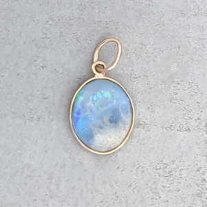 May include: A gold pendant with a round, iridescent opal gemstone. The opal is a light blue color with hints of green and purple.