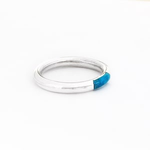 May include: A silver ring with a turquoise inlay. The ring is simple and elegant.