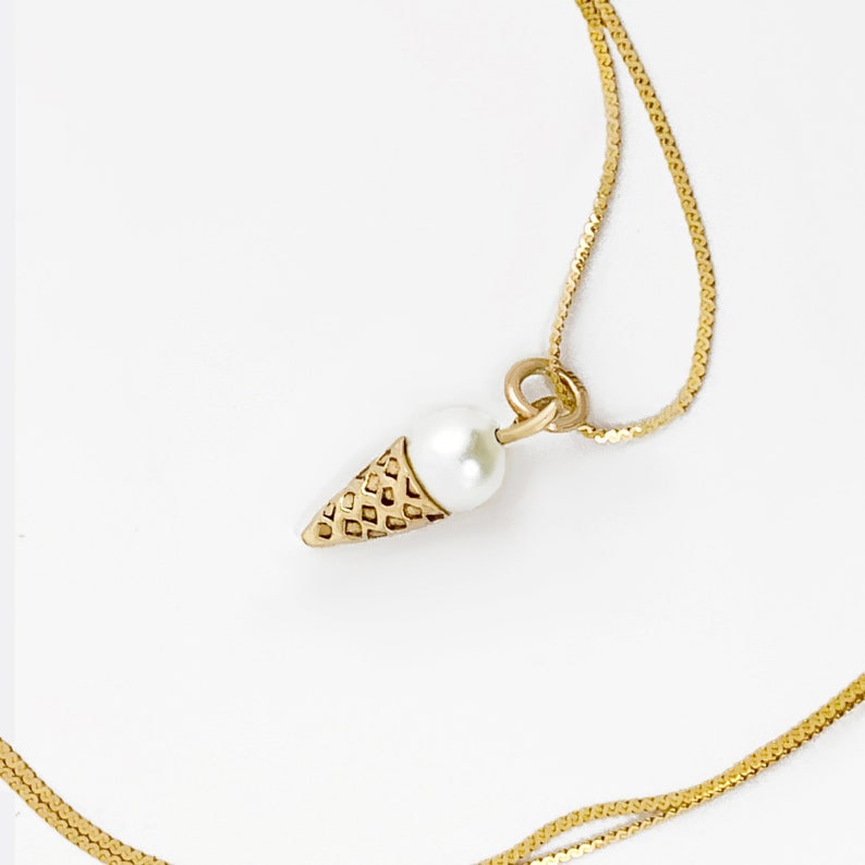 May include: A gold chain necklace with a small pearl and gold ice cream cone pendant.
