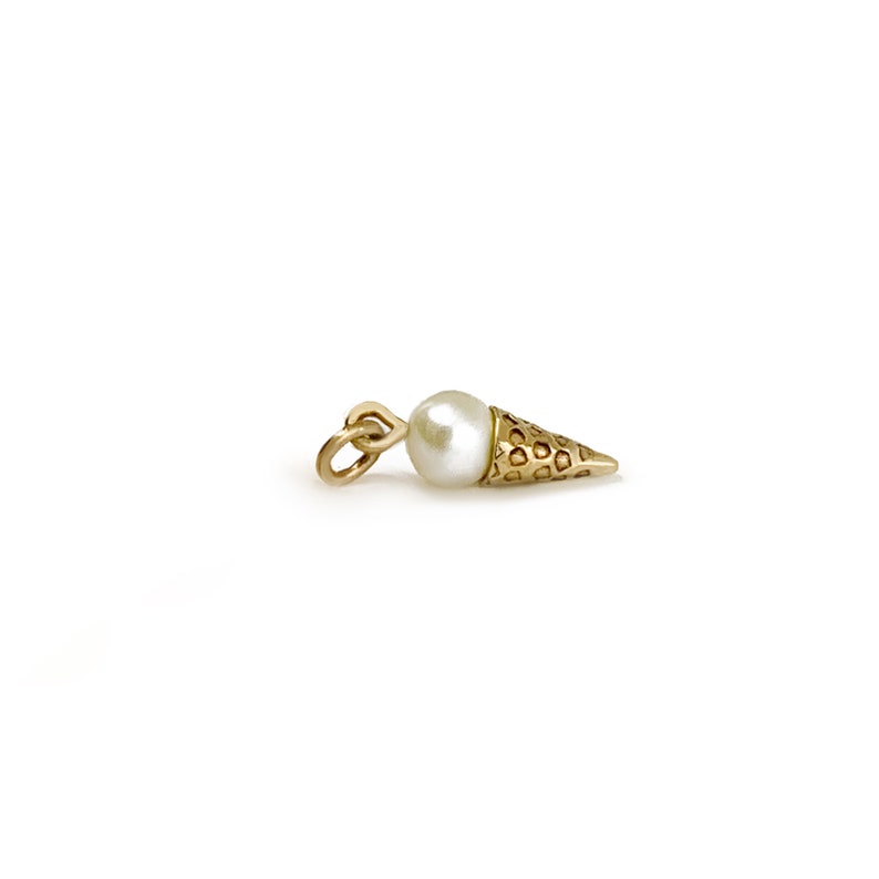 May include: A gold charm in the shape of an ice cream cone with a white pearl on top.