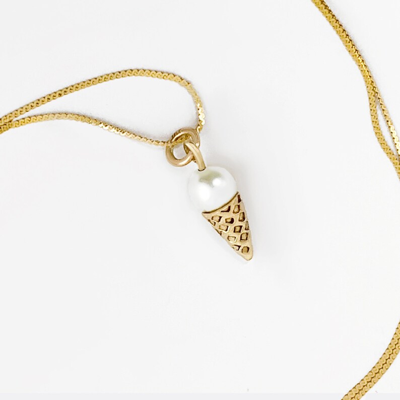 May include: A gold chain necklace with a pearl and gold ice cream cone pendant.