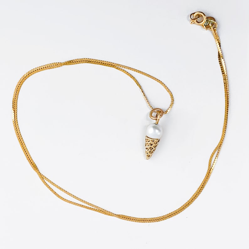 May include: A gold chain necklace with a pearl and gold ice cream cone pendant.