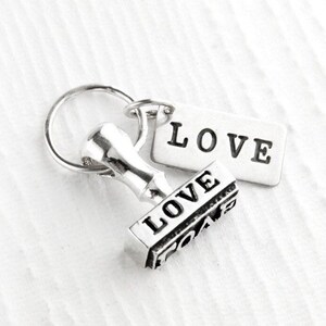May include: Silver keychain with a small, detailed, silver stamp that reads "LOVE" and a silver tag that reads "LOVE".