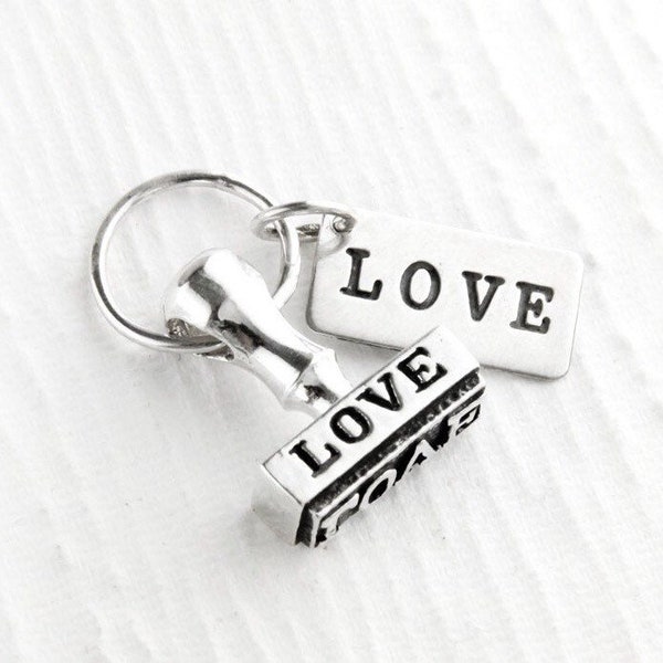 May include: Silver keychain with a small, detailed, silver stamp that reads "LOVE" and a silver tag that reads "LOVE".