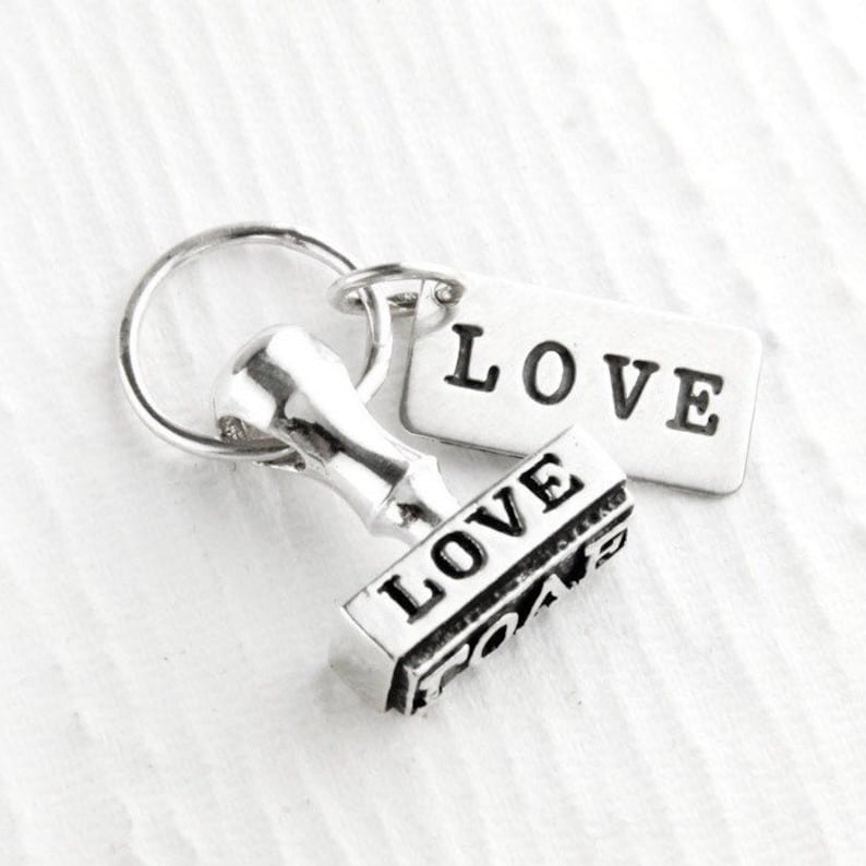 May include: Silver keychain with a small, detailed, silver stamp that reads "LOVE" and a silver tag that reads "LOVE".