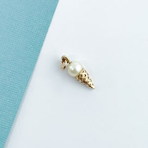 May include: A gold charm in the shape of an ice cream cone with a pearl on top.