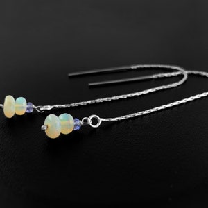 Può includere: Un paio di orecchini a catena d'argento con due perle di opale bianco e una piccola perla blu su ogni orecchino.