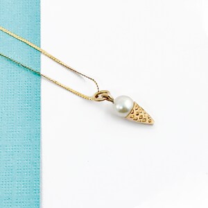 May include: A gold chain necklace with a pearl and gold ice cream cone pendant.