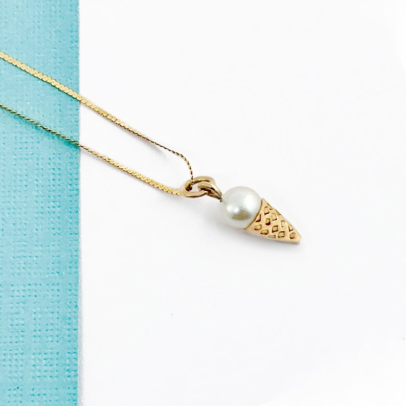 May include: A gold chain necklace with a pearl and gold ice cream cone pendant.