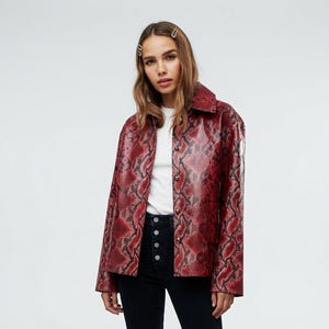 May include: A red and black snakeskin-patterned button-down jacket worn over a plain white t-shirt, paired with black high-waisted denim jeans featuring a visible button fly and black leather ankle boots with a block heel.