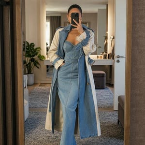 May include: A long denim dress with a sweetheart neckline and a fitted bodice, layered under a beige trench coat with denim lapels and cuffs. The ensemble is paired with pointed-toe white heels, creating a structured and layered appearance.