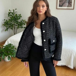 May include: A black tweed jacket with white buttons and faux fur trim. The jacket has a quilted lining and two front pockets. The model is wearing a white tank top and black pants.