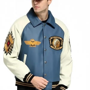 May include: A blue and cream-colored varsity jacket with a button-up front. The jacket features a patch with the text "BIG CHIEF CURTIS" and an eagle emblem. The left sleeve has a geometric design. The jacket has black and gold striped cuffs and hem.