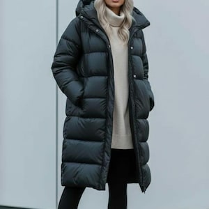 May include: A long, black puffer coat with a hood, worn over a cream-coloured sweater and black leggings. The outfit is completed with a white beanie and light-coloured boots. The coat appears to be knee-length.